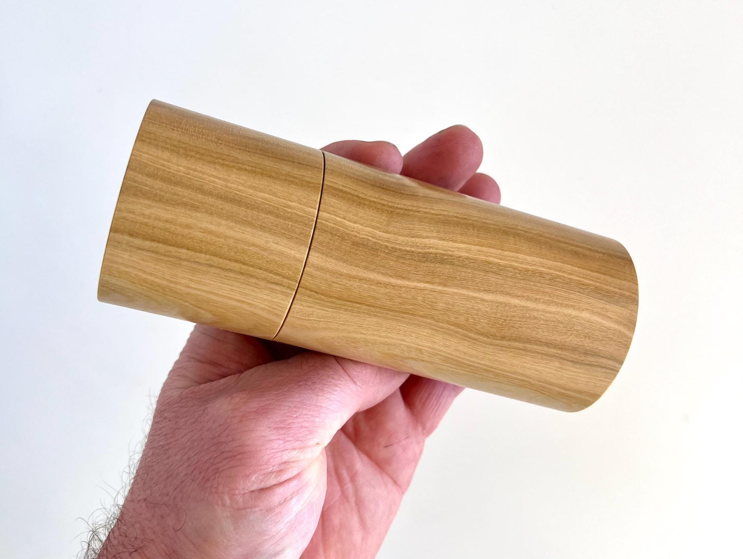 Mans hand holding single straight cylindrical Wilga timber grinder