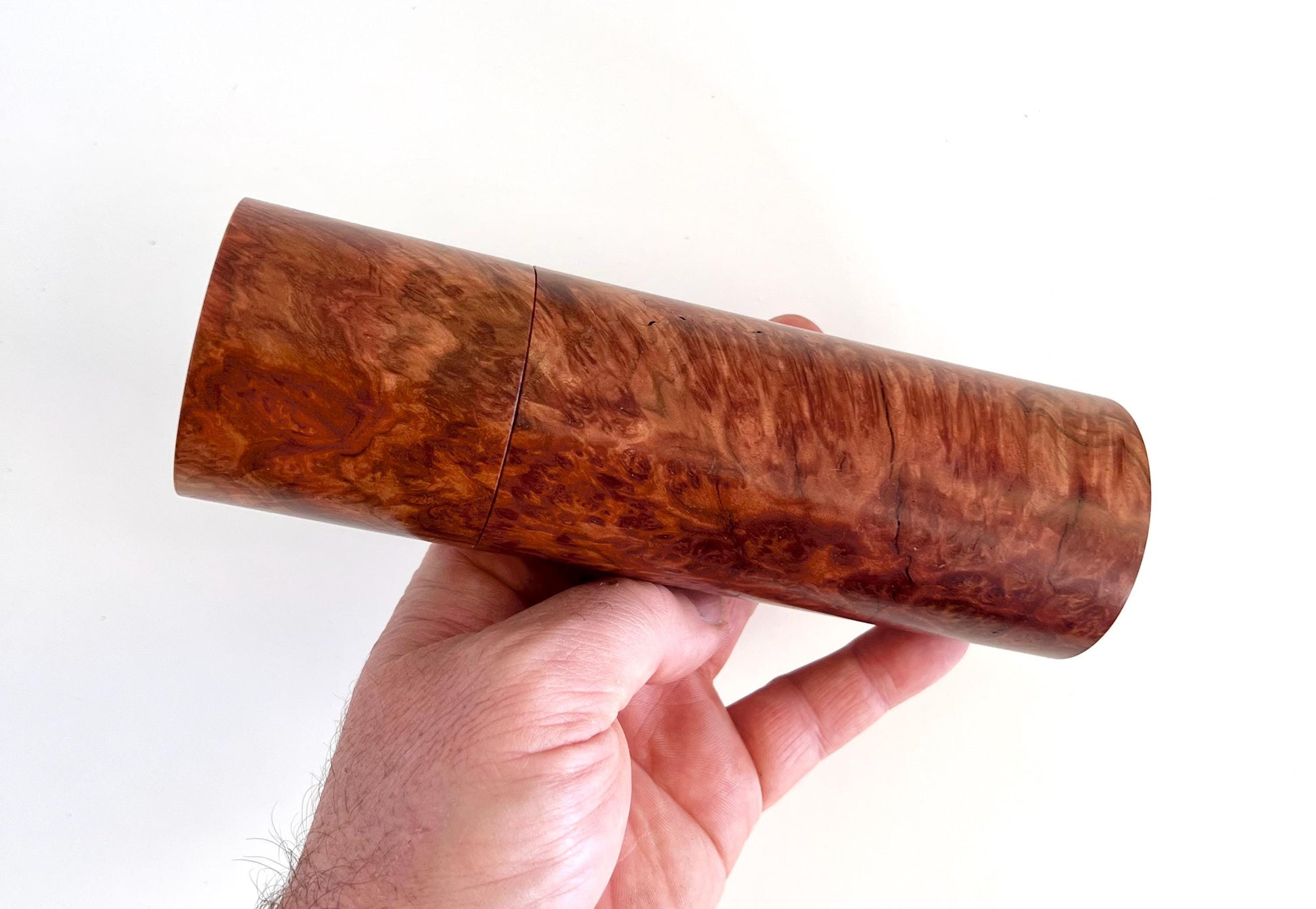 Mans hand holding single straight cylindrical Red Mallee burl timber grinder