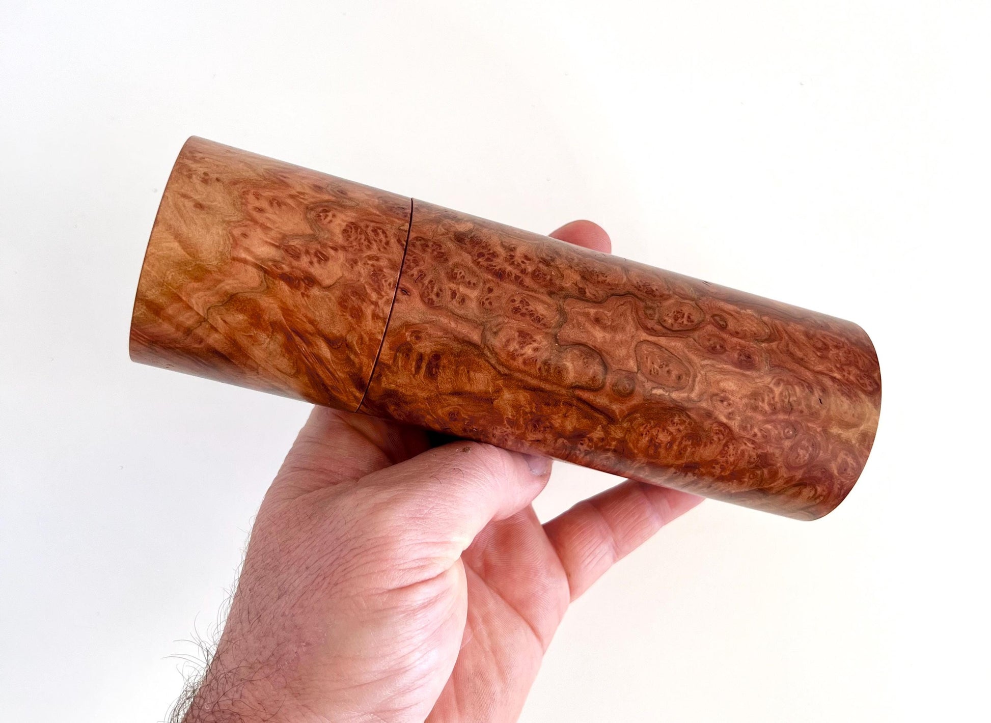 Mans hand holding single straight cylindrical Red Mallee burl timber grinder