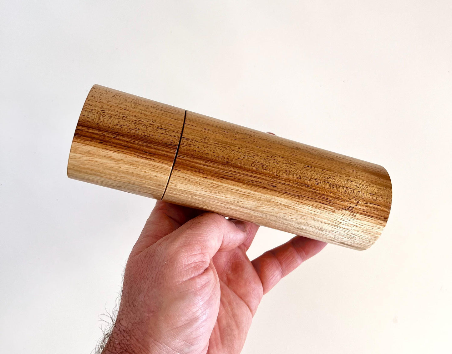 Mans hand holding single straight cylindrical Blackwood timber grinder