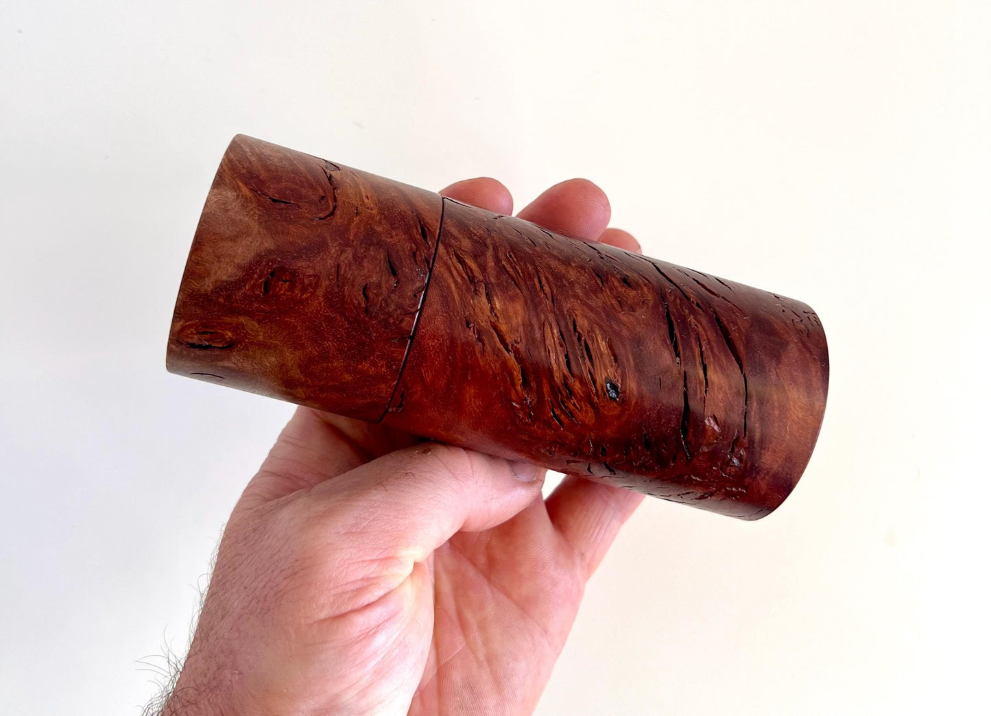 Mans hand holding single straight cylindrical Jarrah burl timber grinder