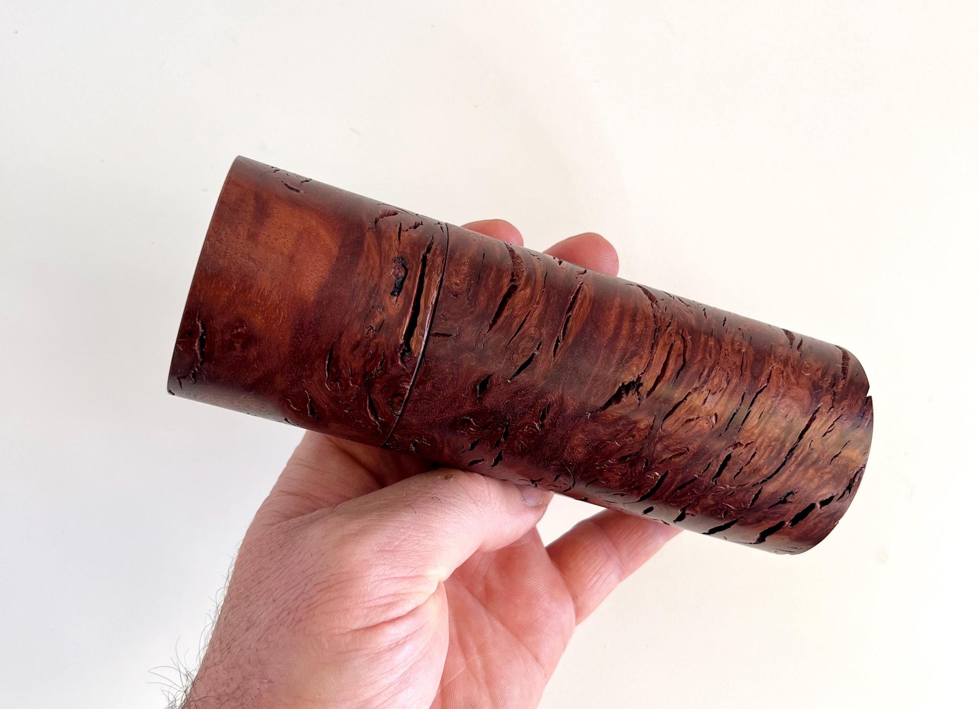 Mans hand holding single straight cylindrical Jarrah burl timber grinder