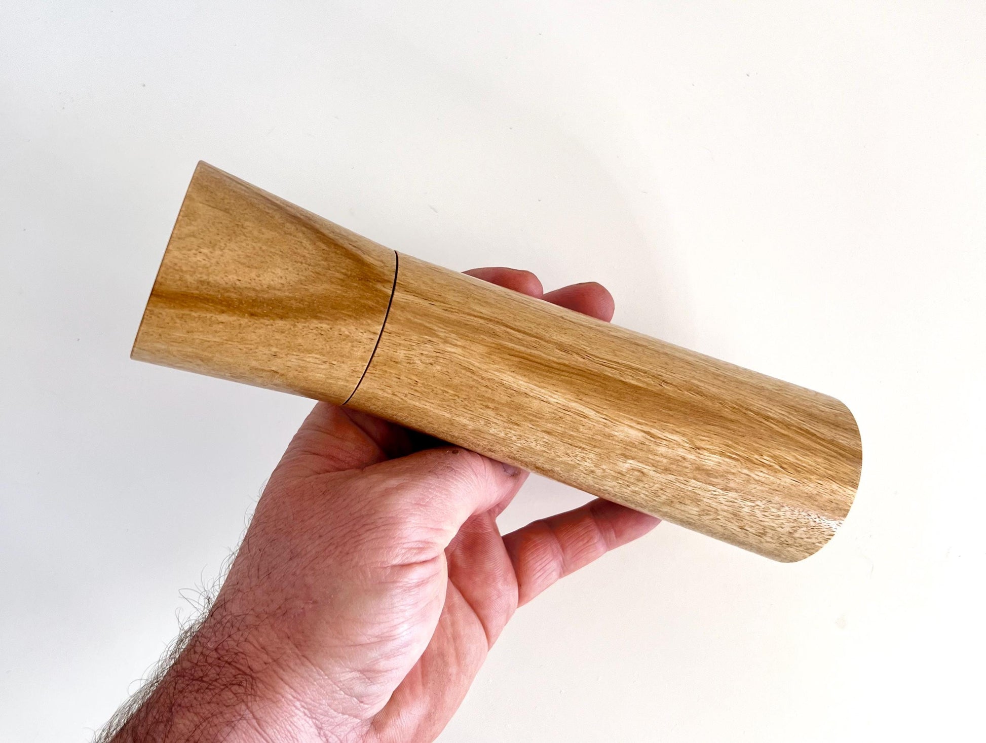 Mans hand holding single straight cylindrical bluegum timber grinder