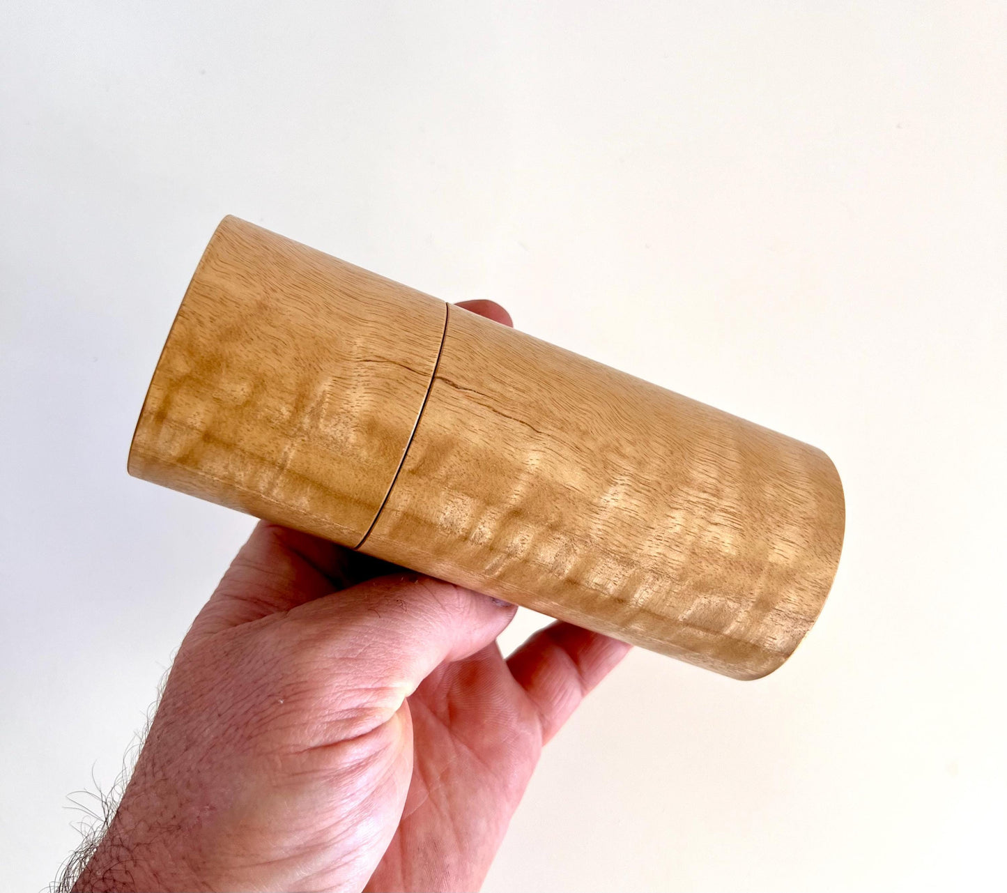 Mans hand holding single straight cylindrical Marri timber grinder