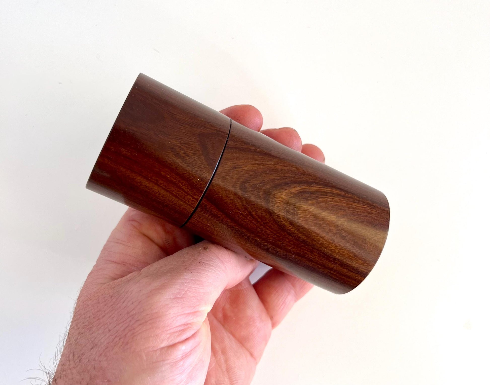 Mans hand holding single straight cylindrical Gidgee timber grinder