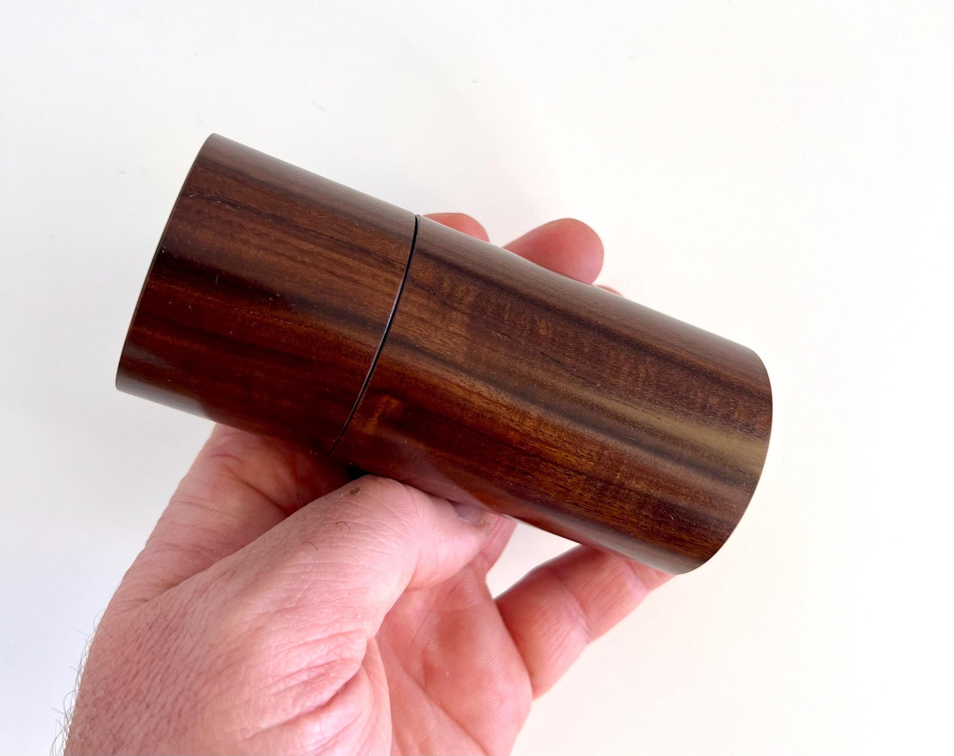 Mans hand holding single straight cylindrical Gidgee timber grinder