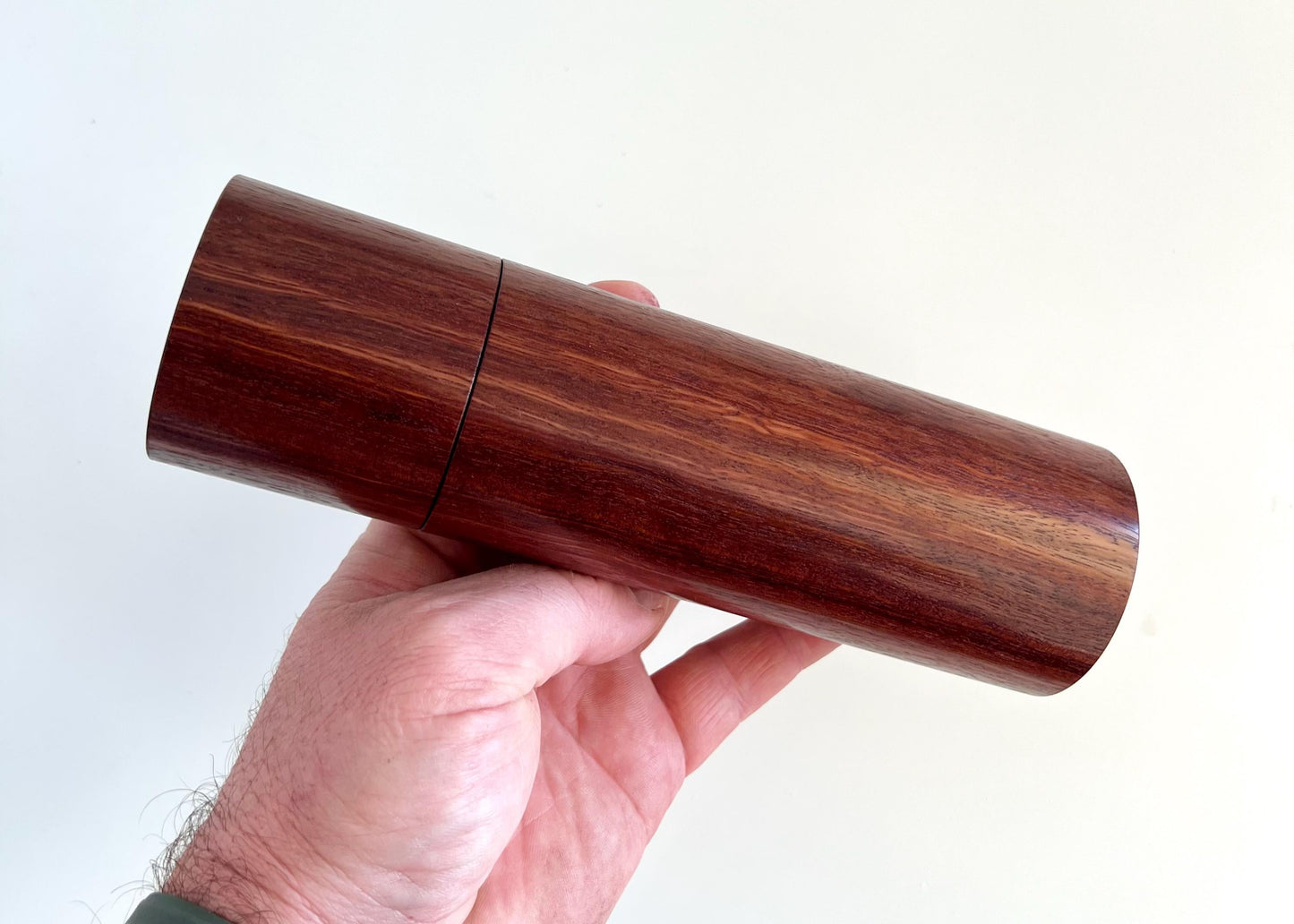 Mans hand holding single cylindrical Jarrah timber grinder