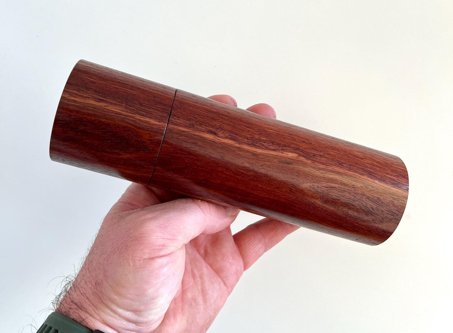 Mans hand holding single cylindrical Jarrah timber grinder