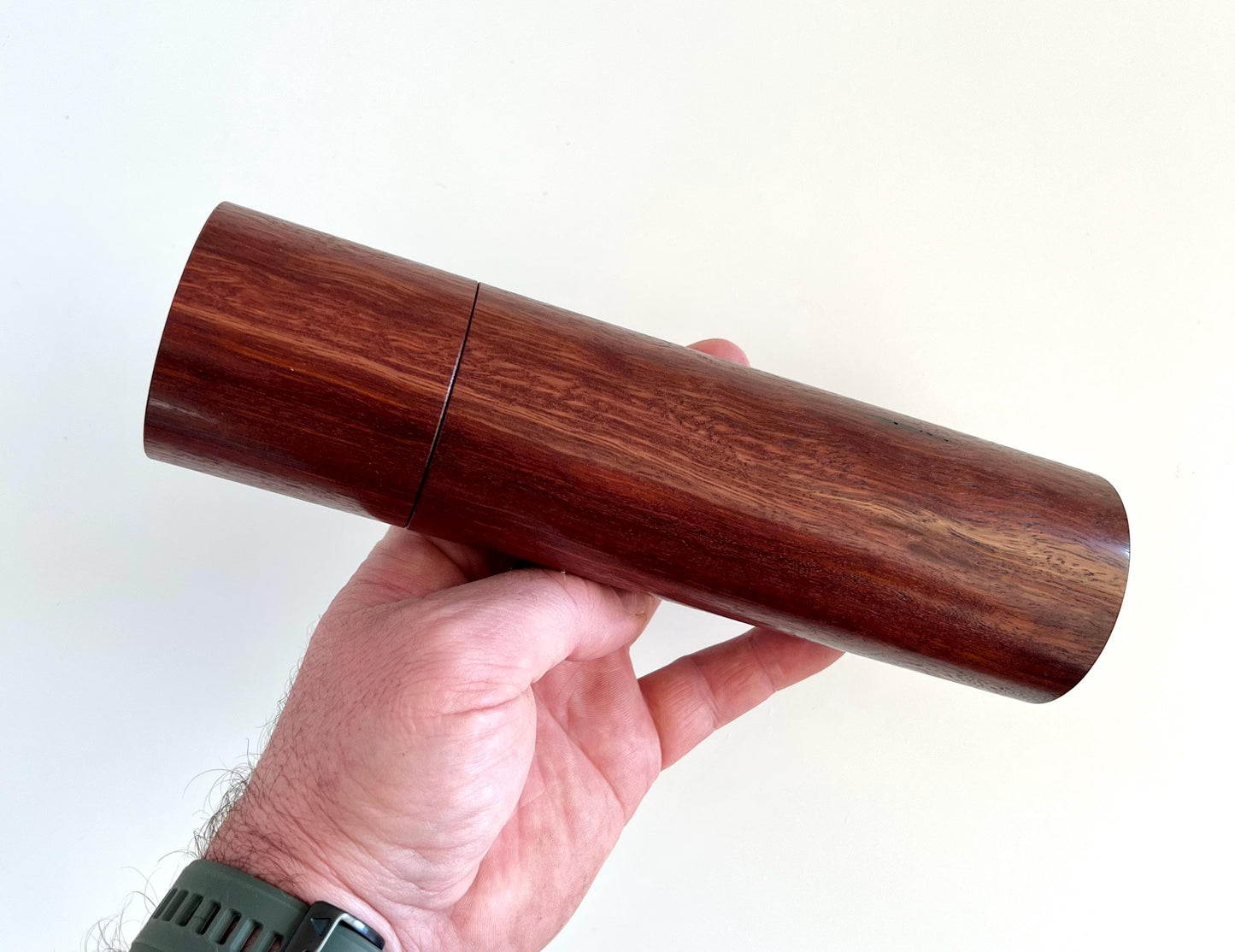 Mans hand holding single cylindrical Jarrah timber grinder