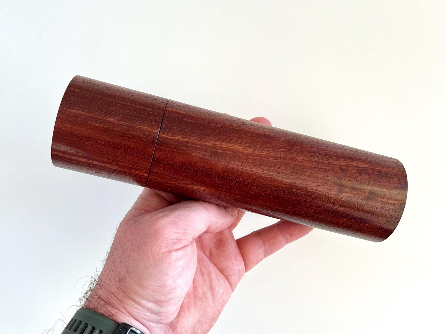 Mans hand holding single cylindrical Jarrah timber grinder