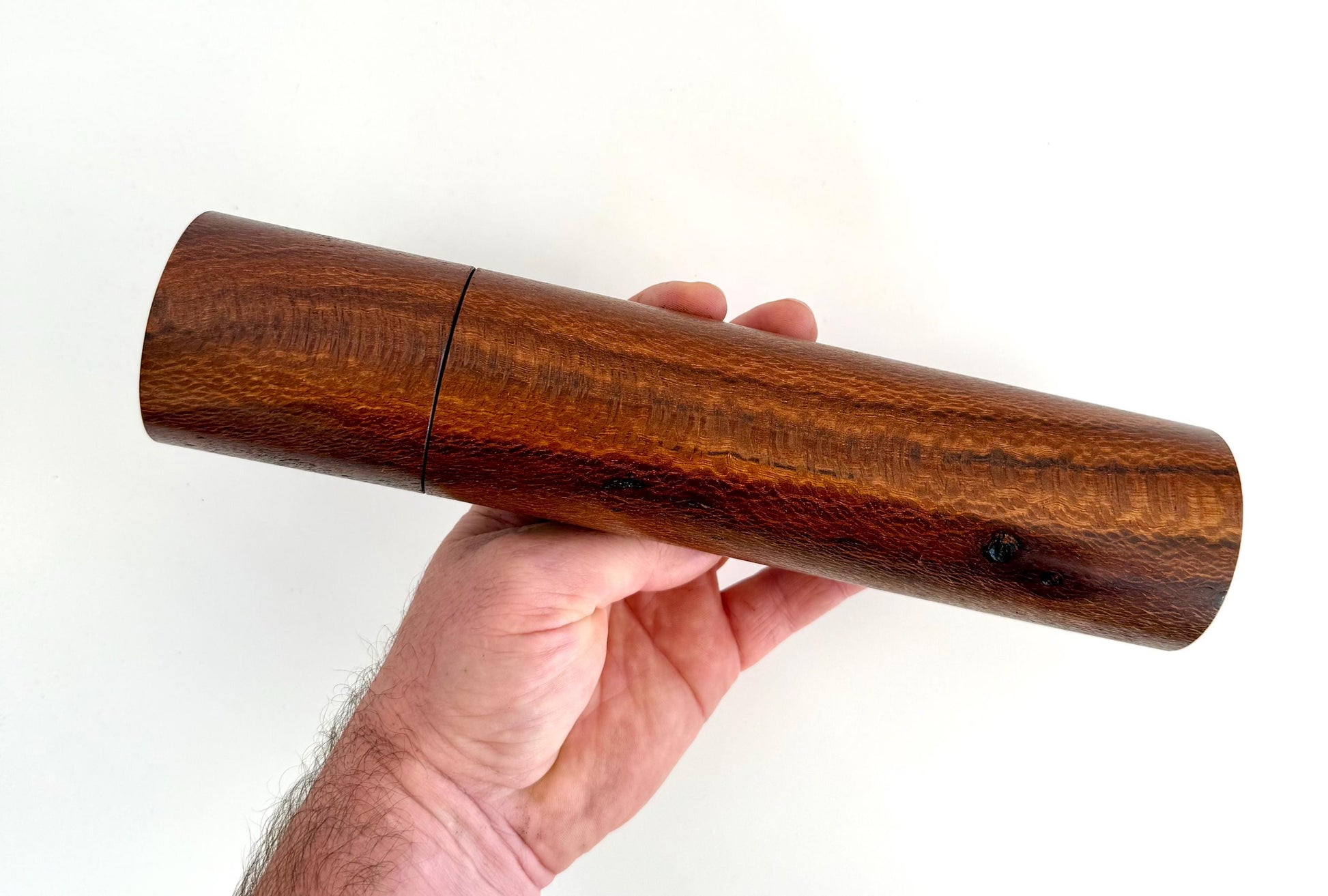 Mans hand holding single straight cylindrical Banksia timber grinder