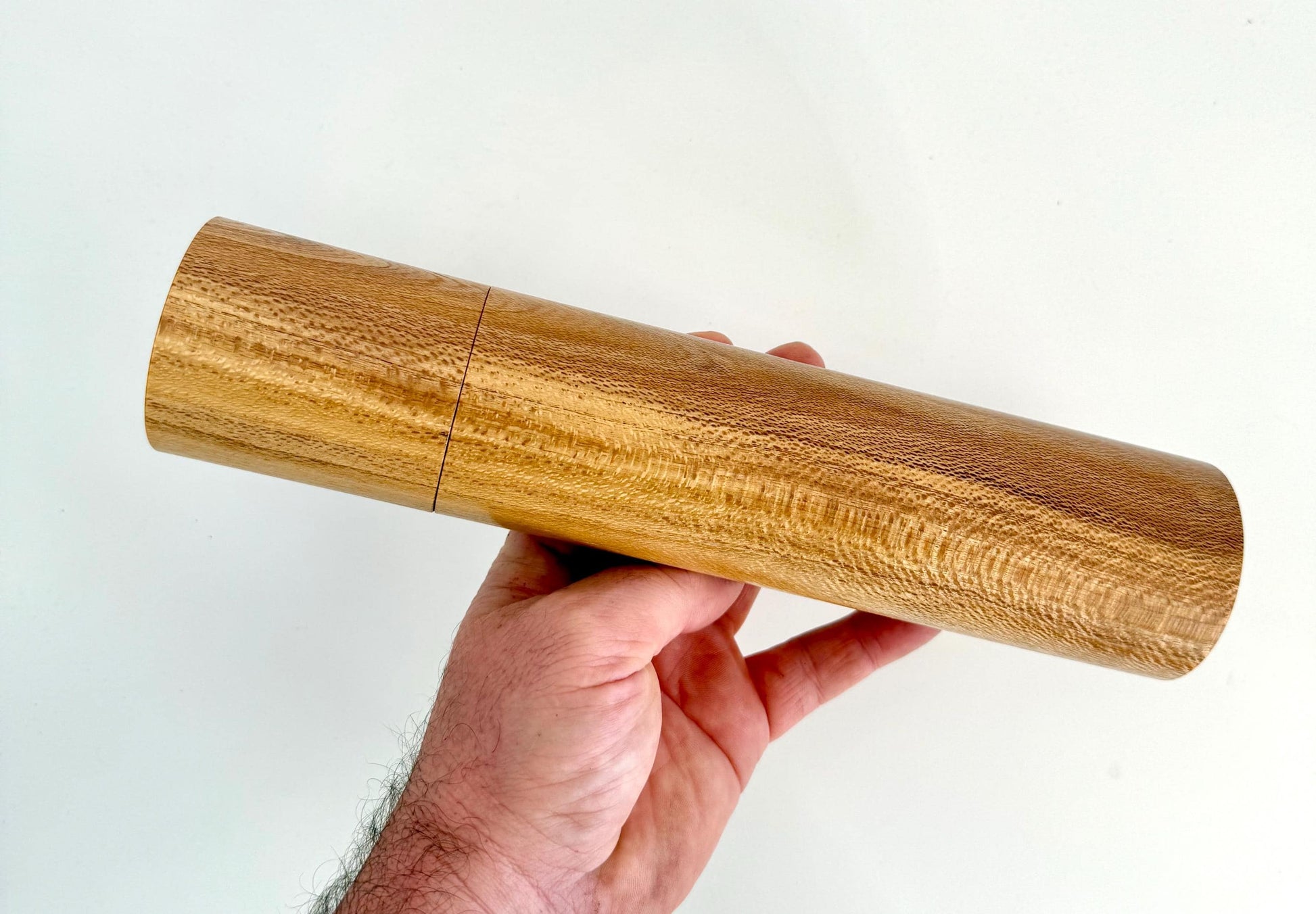 Mans hand holding single straight cylindrical Banksia timber grinder