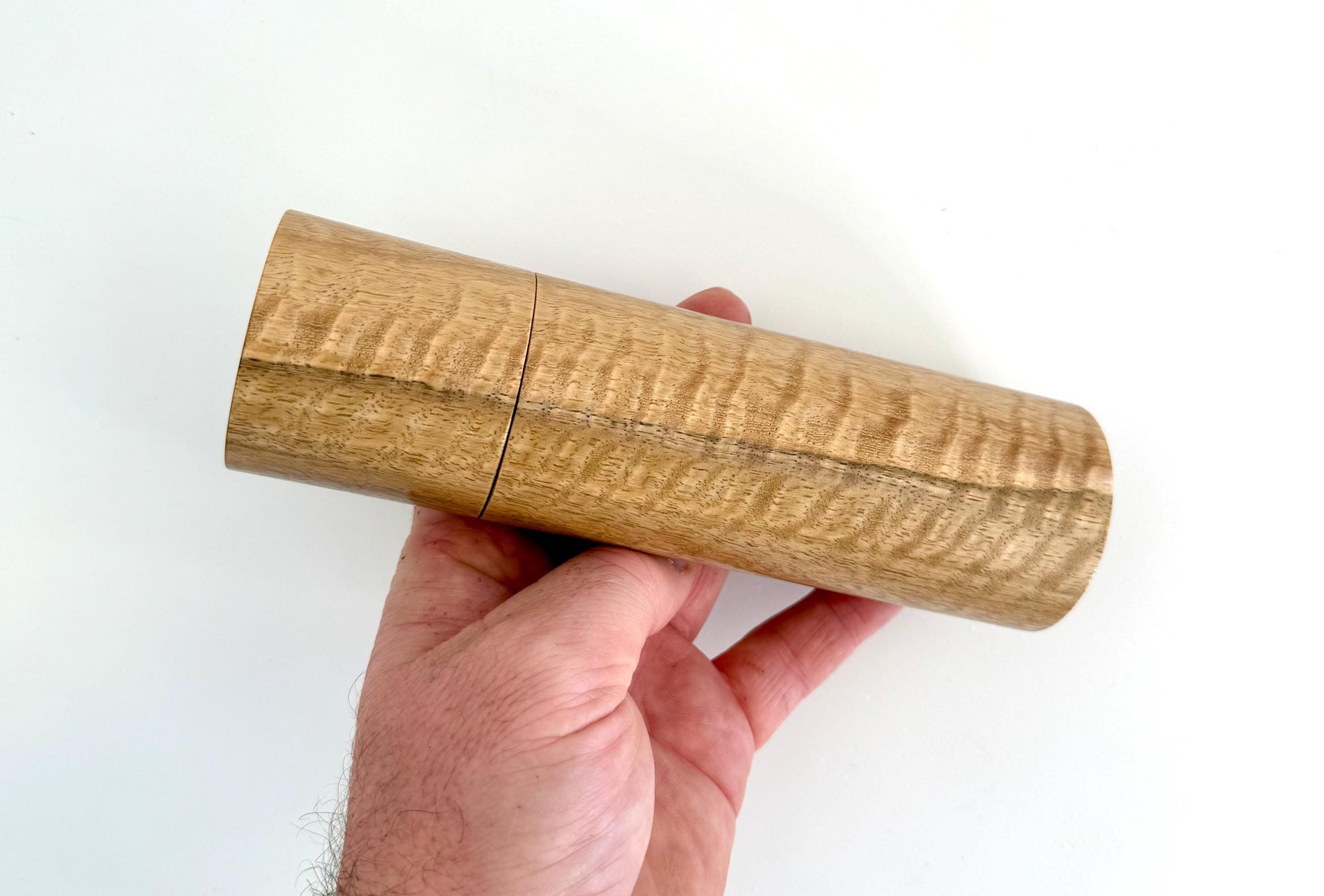 Mans hand holding single straight cylindrical Marri timber grinder