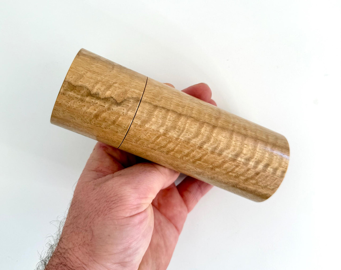 Mans hand holding single straight cylindrical Marri timber grinder