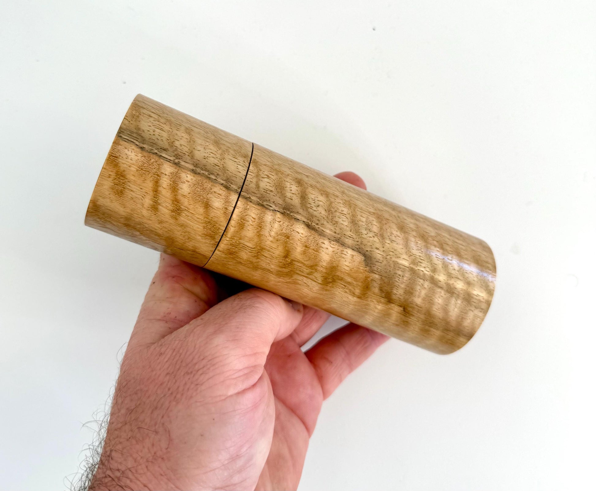 Mans hand holding single straight cylindrical Marri timber grinder