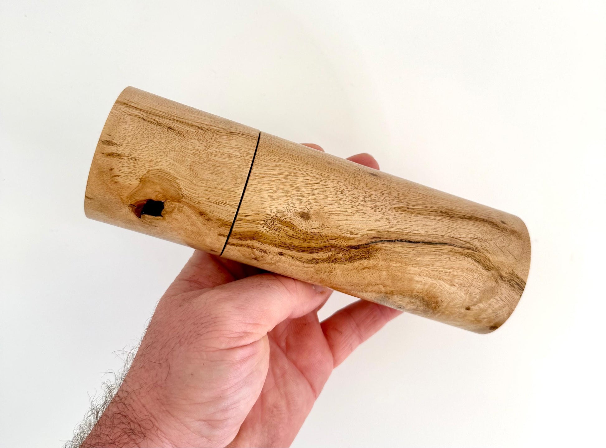 Mans hand holding single straight cylindrical Lemon scented gum timber grinder