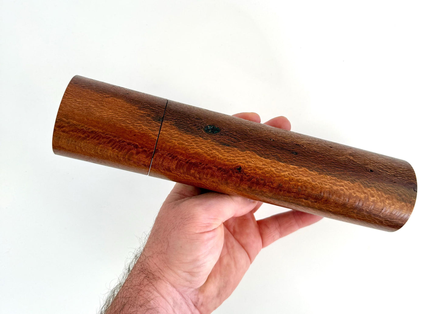 Mans hand holding single straight cylindrical Banksia timber grinder