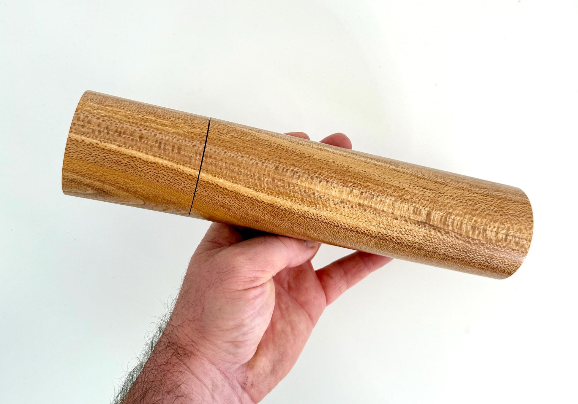 Mans hand holding single straight cylindrical Banksia timber grinder