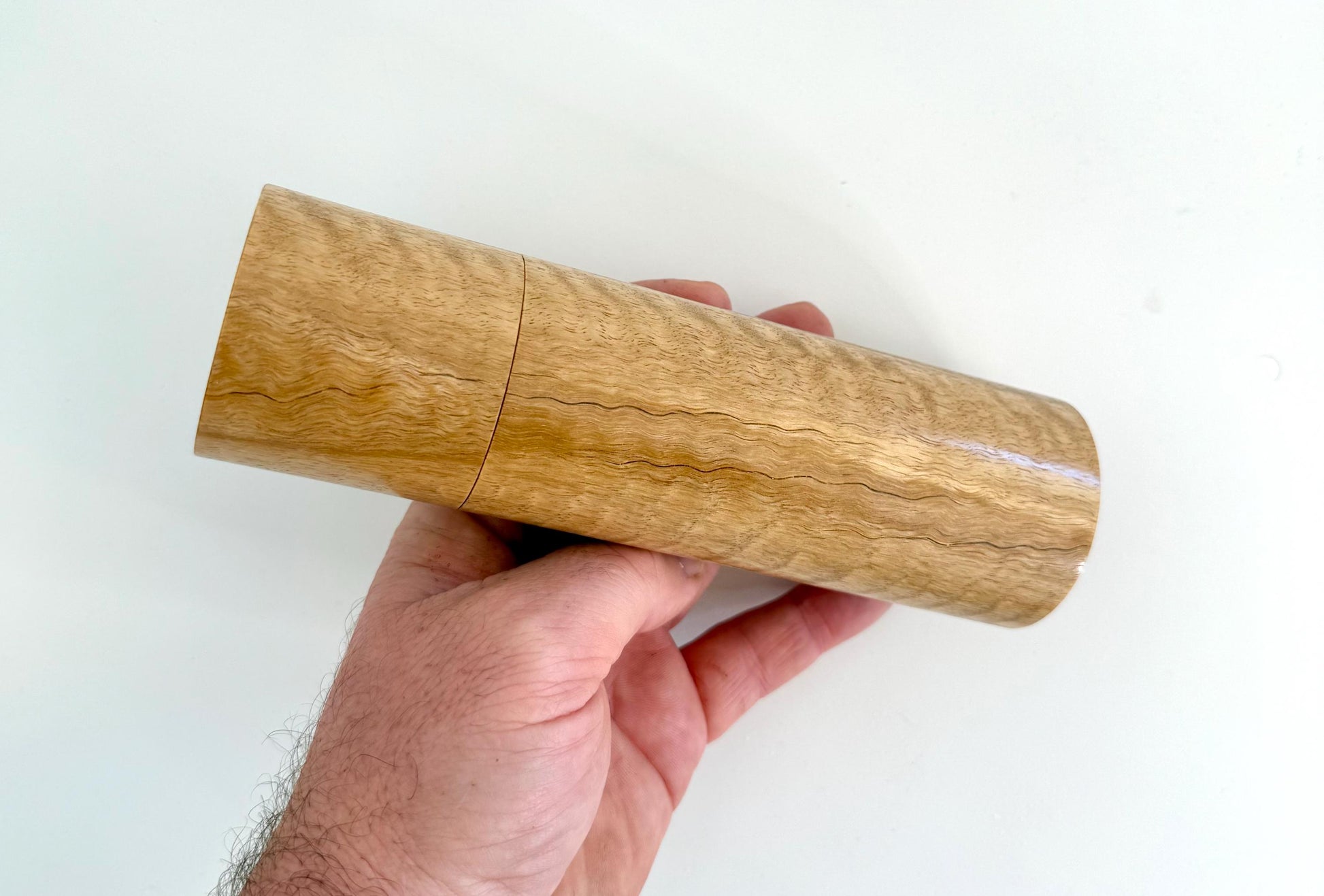 Mans hand holding single straight cylindrical Marri timber grinder