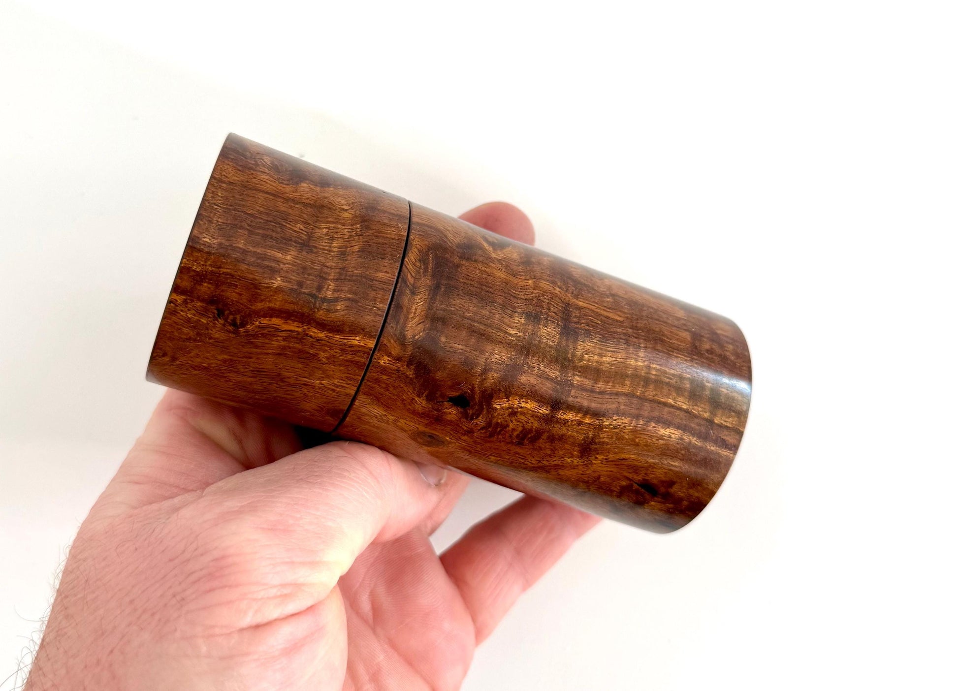 Mans hand holding single straight cylindrical Black Mulga timber grinder