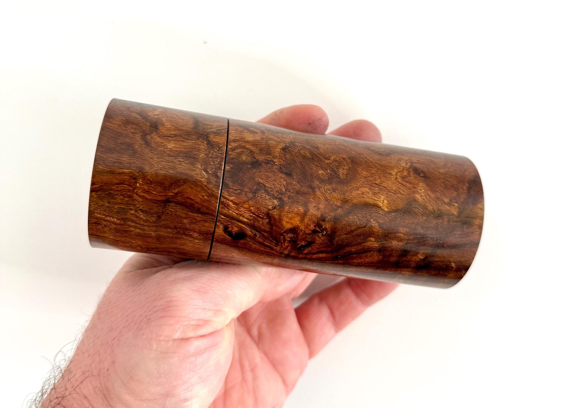 Mans hand holding single straight cylindrical Black Mulga timber grinder