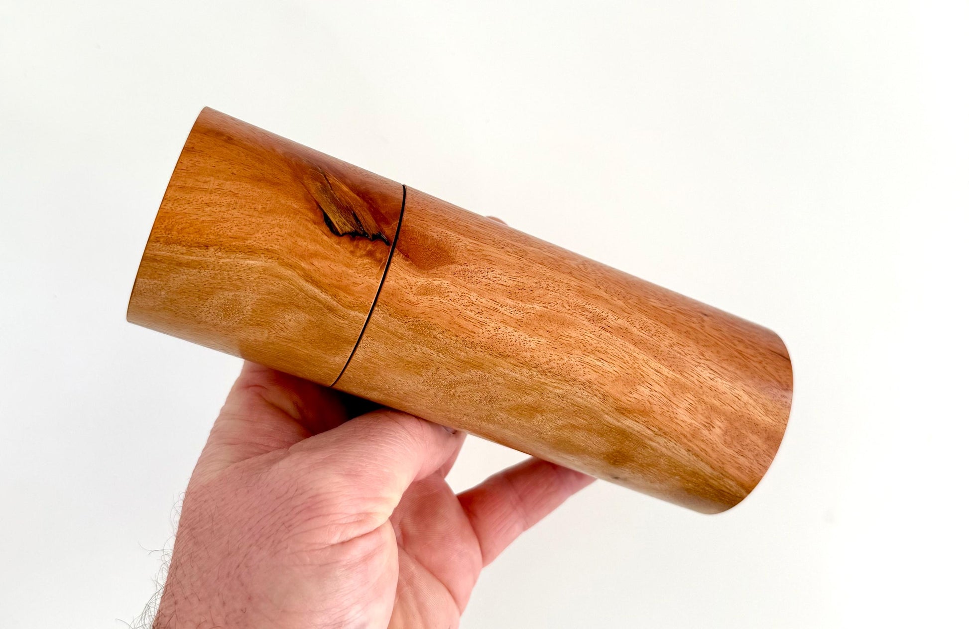 Mans hand holding single straight cylindrical River Red Gum timber grinder