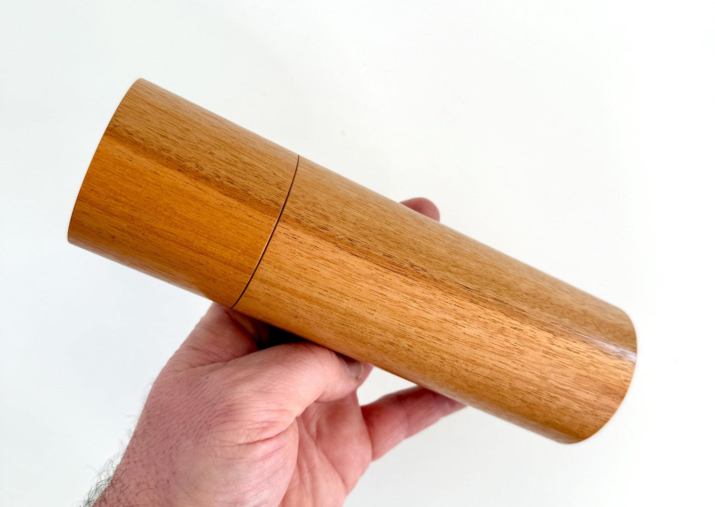 Mans hand holding single straight cylindrical River Red Gum timber grinder