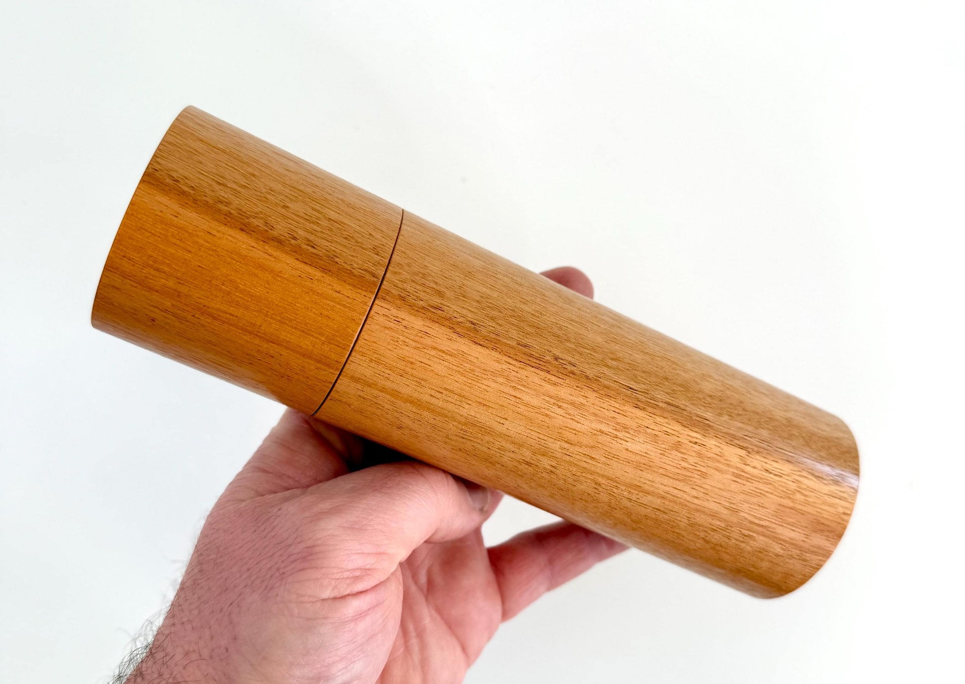Mans hand holding single straight cylindrical River Red Gum timber grinder