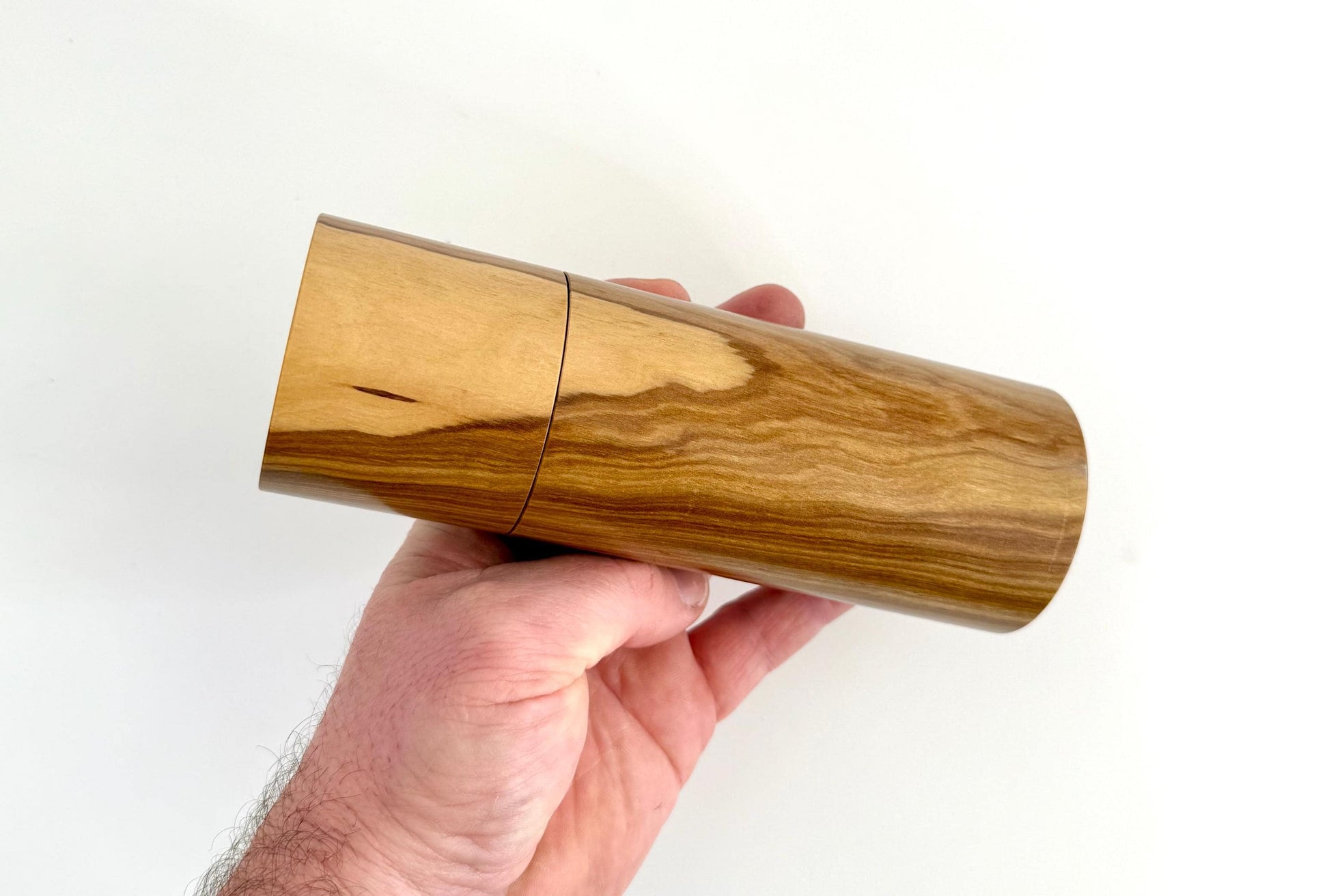 Mans hand holding single straight cylindrical Buddha timber grinder
