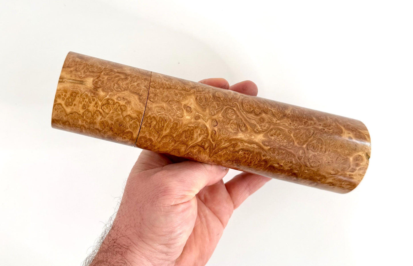 Mans hand holding single straight cylindrical Red Mallee Burl timber grinder