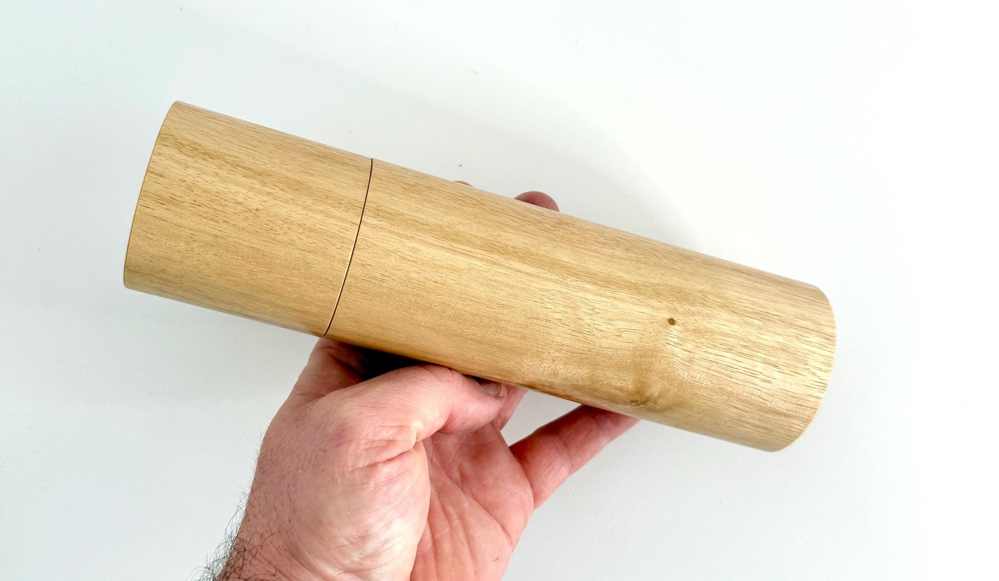 Mans hand holding single straight cylindrical Blackbutt timber grinder