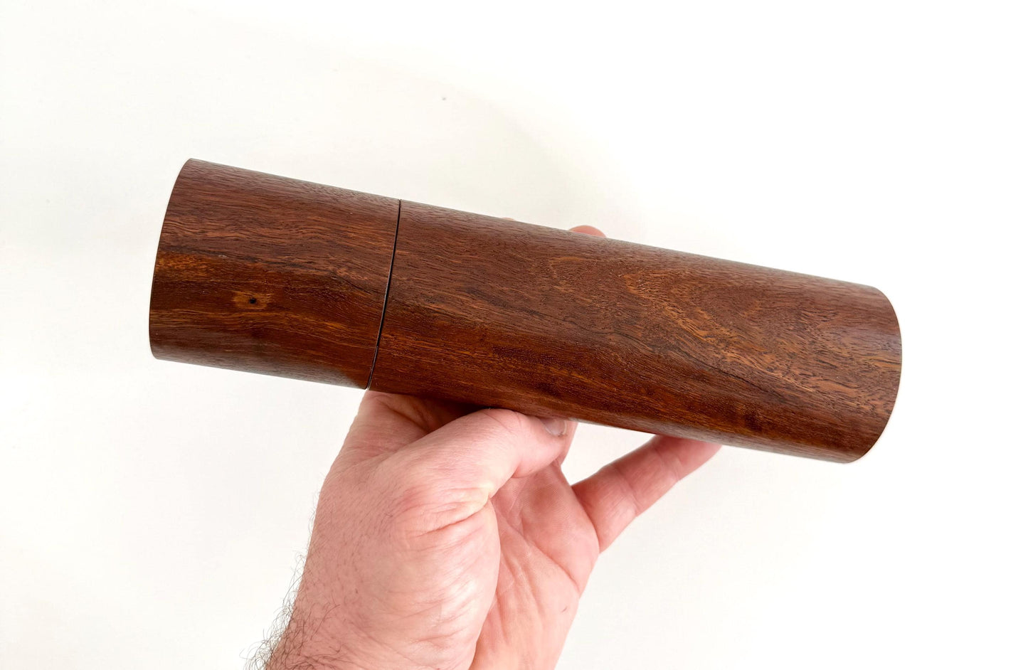 Mans hand holding single straight cylindrical Jarrah timber grinder
