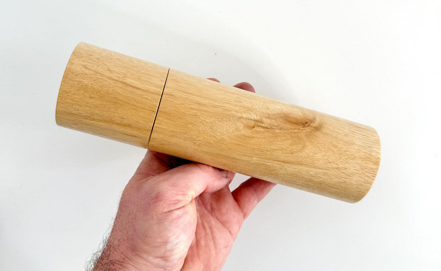 Mans hand holding single straight cylindrical Blackbutt timber grinder