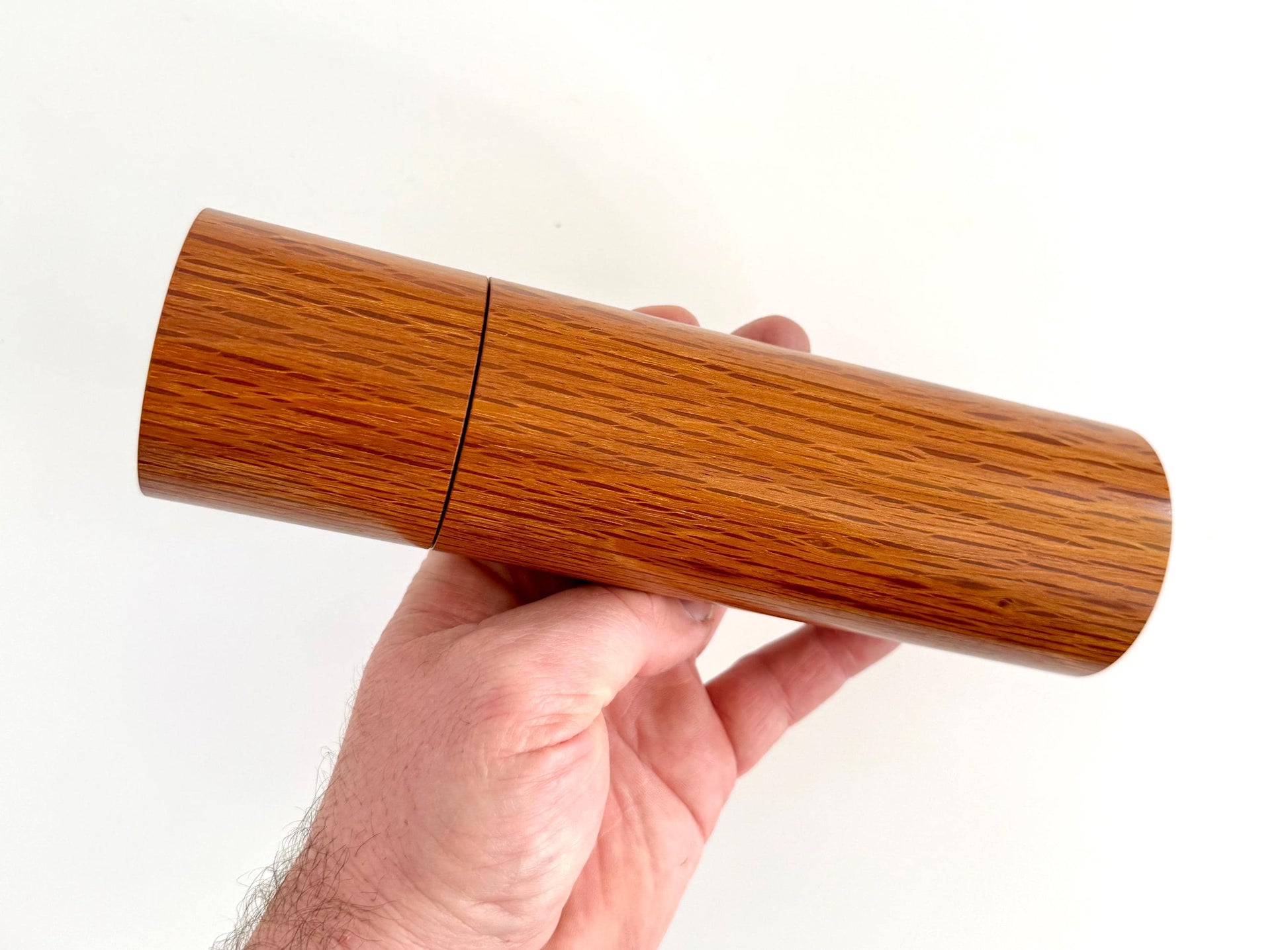 Mans hand holding single straight cylindrical Sheoak timber grinder
