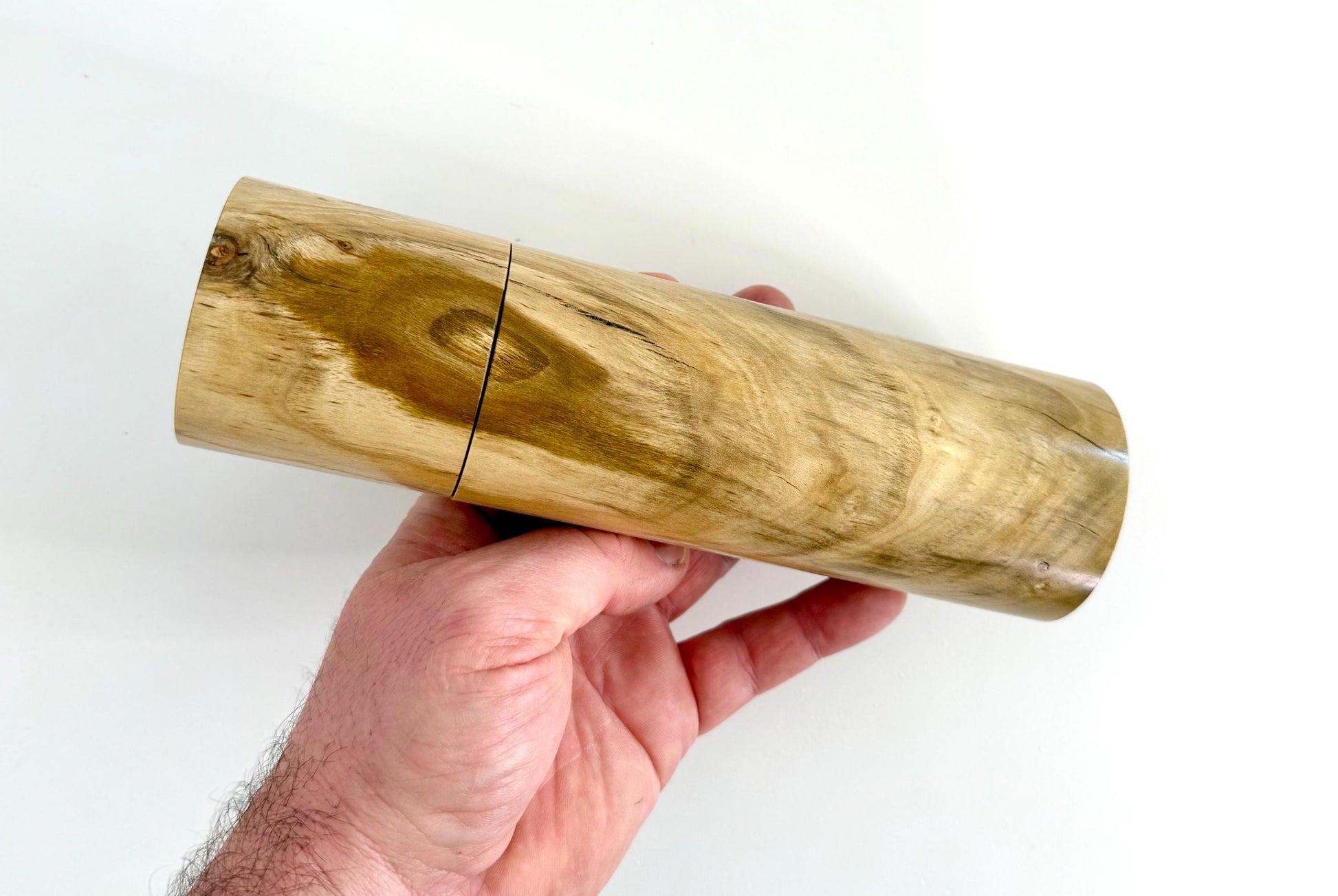 Mans hand holding single straight cylindrical Pistachio timber grinder