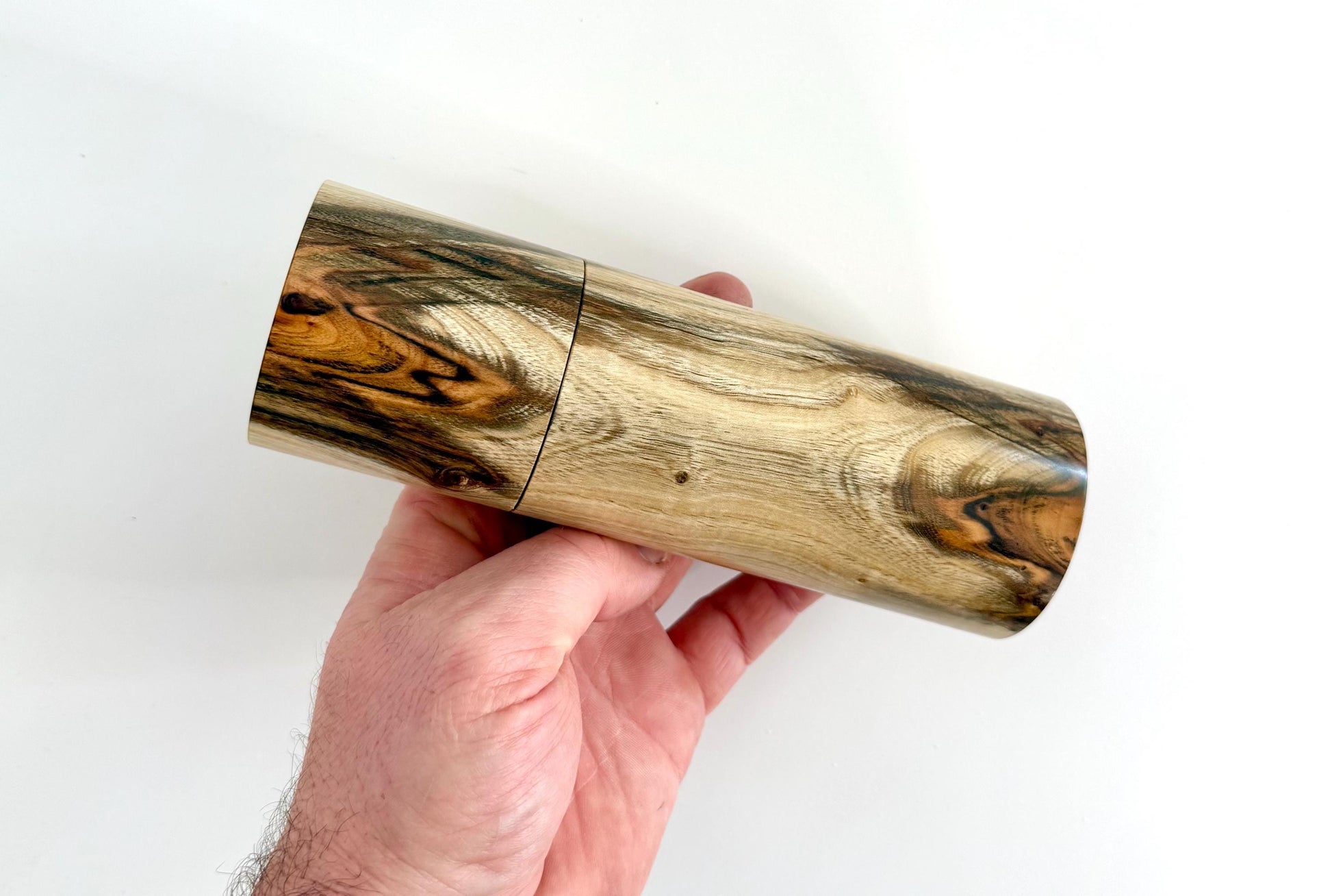 Mans hand holding single straight cylindrical Pistachio timber grinder