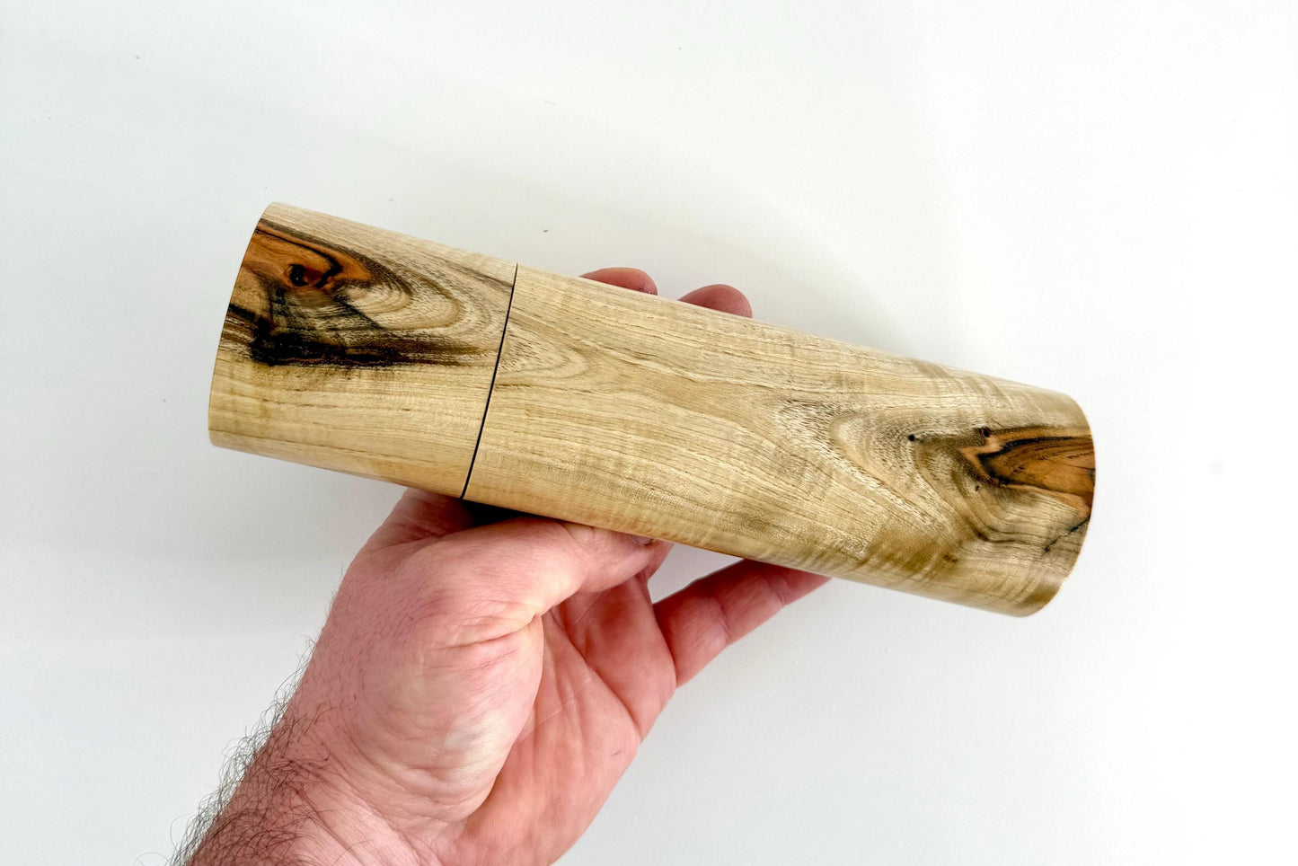 Mans hand holding single straight cylindrical Pistachio timber grinder
