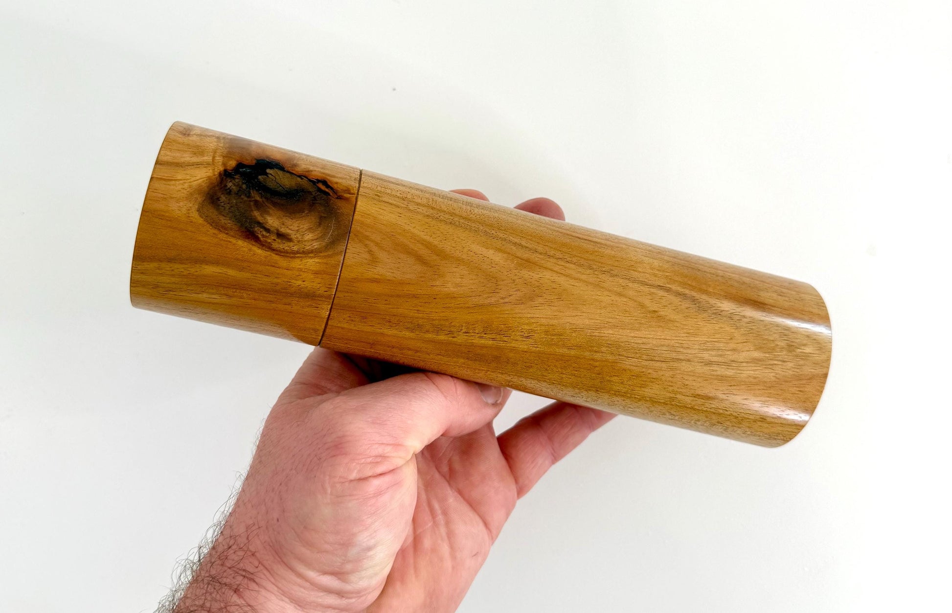 Mans hand holding single straight cylindrical Black Wattle timber grinder