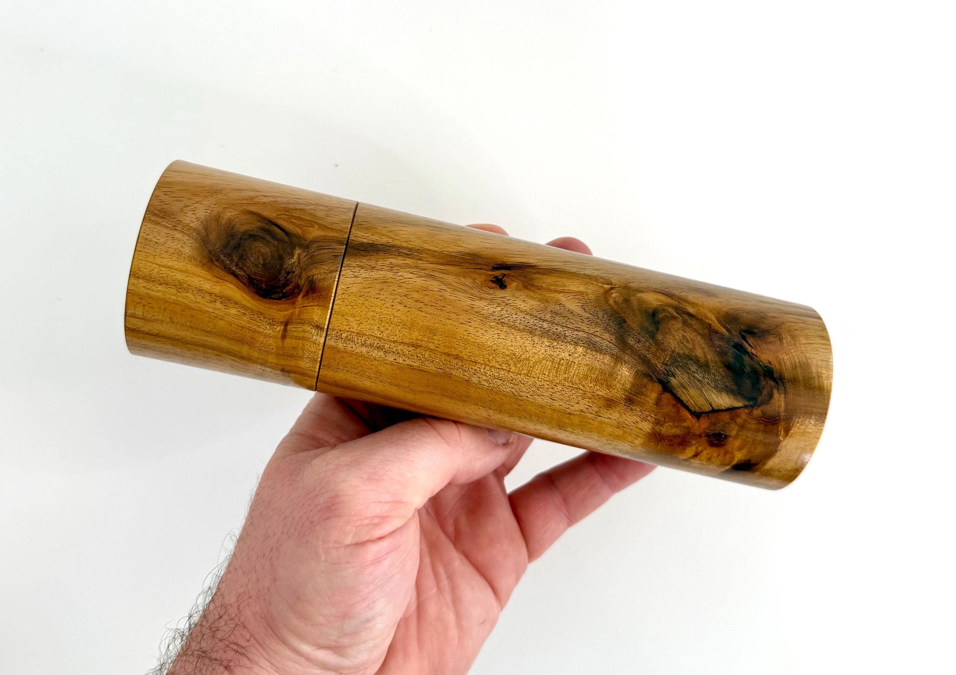 Mans hand holding single straight cylindrical Black Wattle timber grinder