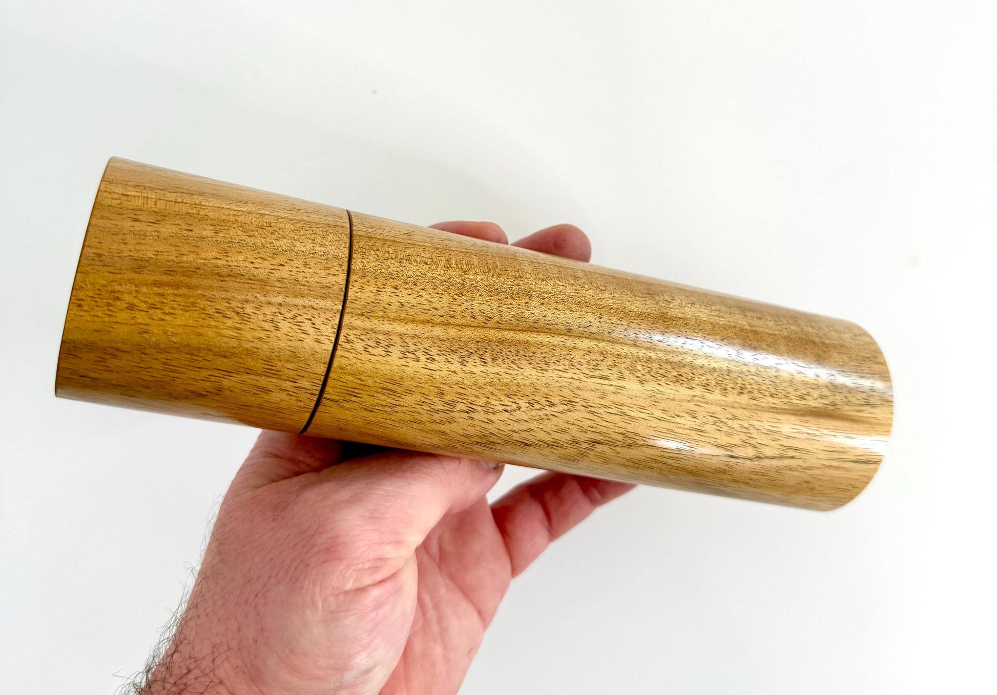 Mans hand holding single straight cylindrical Black Wattle timber grinder