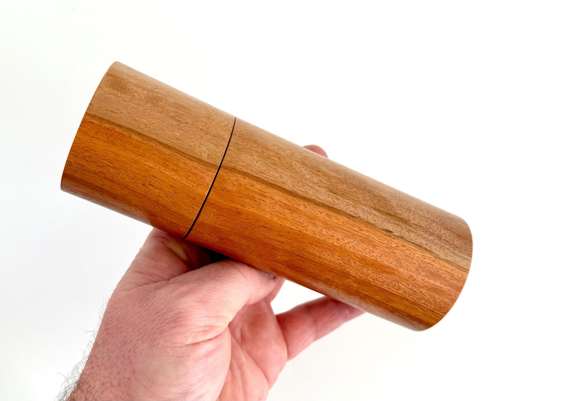 Mans hand holding single straight cylindrical River Red Gum timber grinder