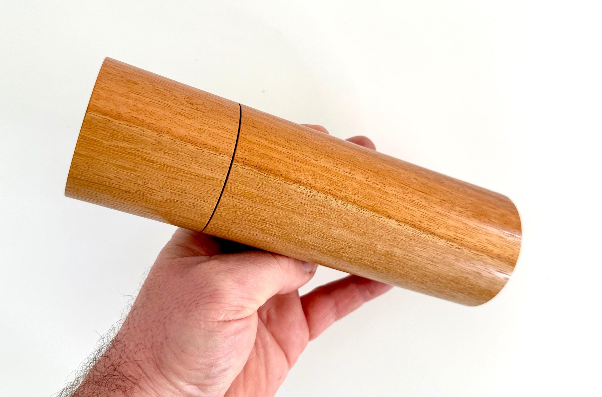 Mans hand holding single straight cylindrical River Red Gum timber grinder