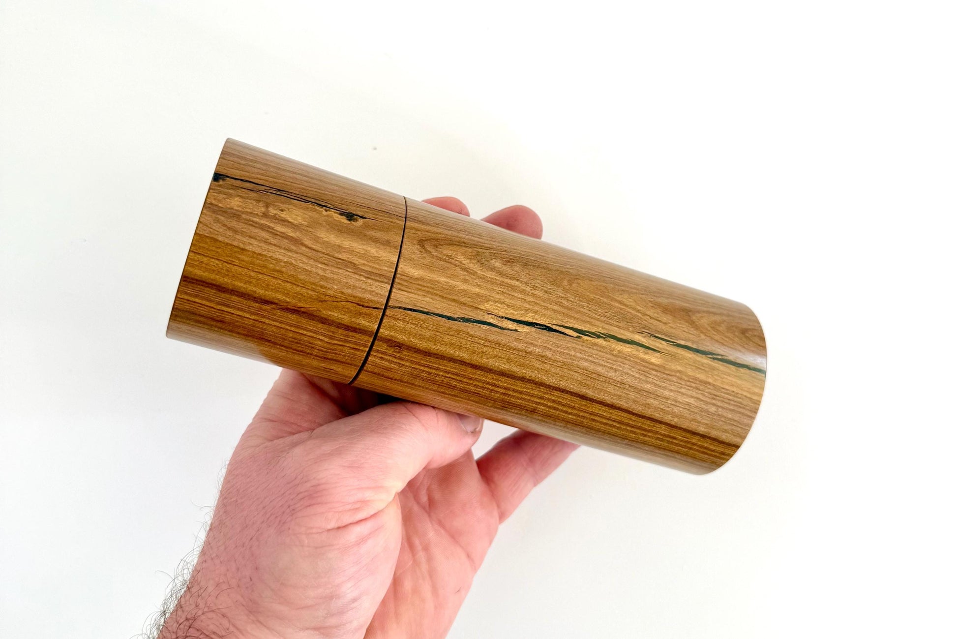 Mans hand holding single straight cylindrical Buddha timber grinder