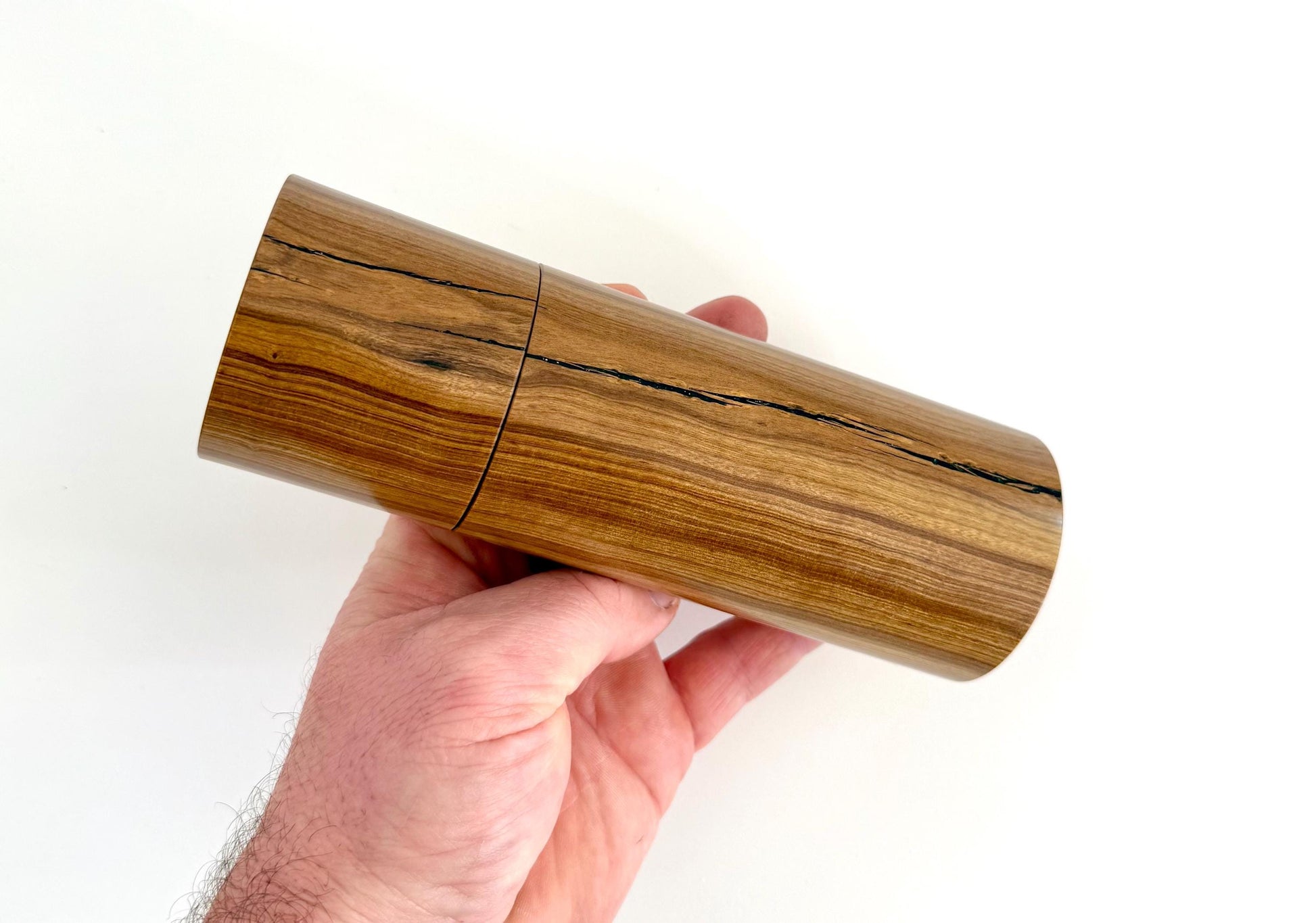 Mans hand holding single straight cylindrical Buddha timber grinder