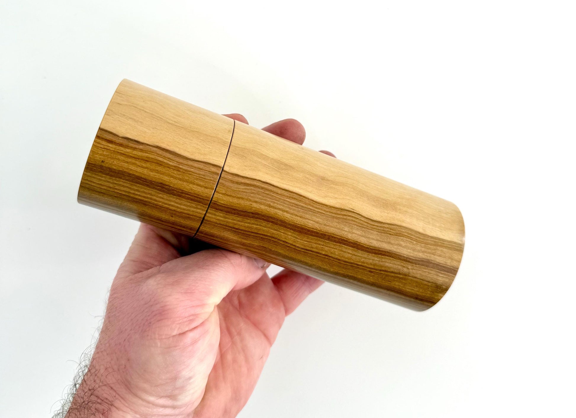 Mans hand holding single straight cylindrical Buddha timber grinder