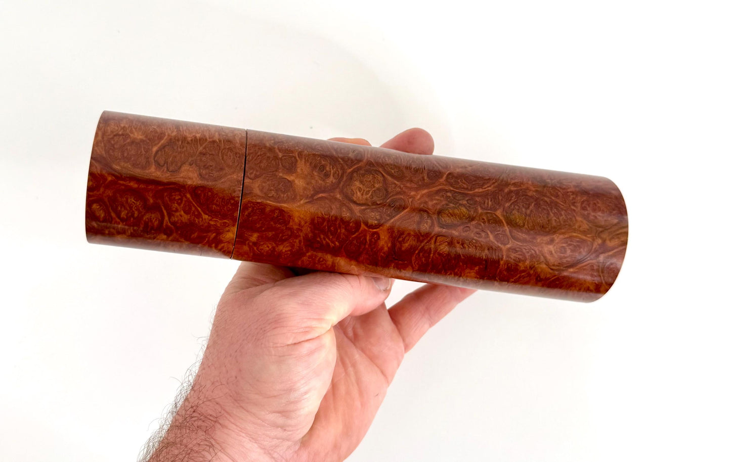 Mans hand holding single straight cylindrical Red Mallee Burl timber grinder