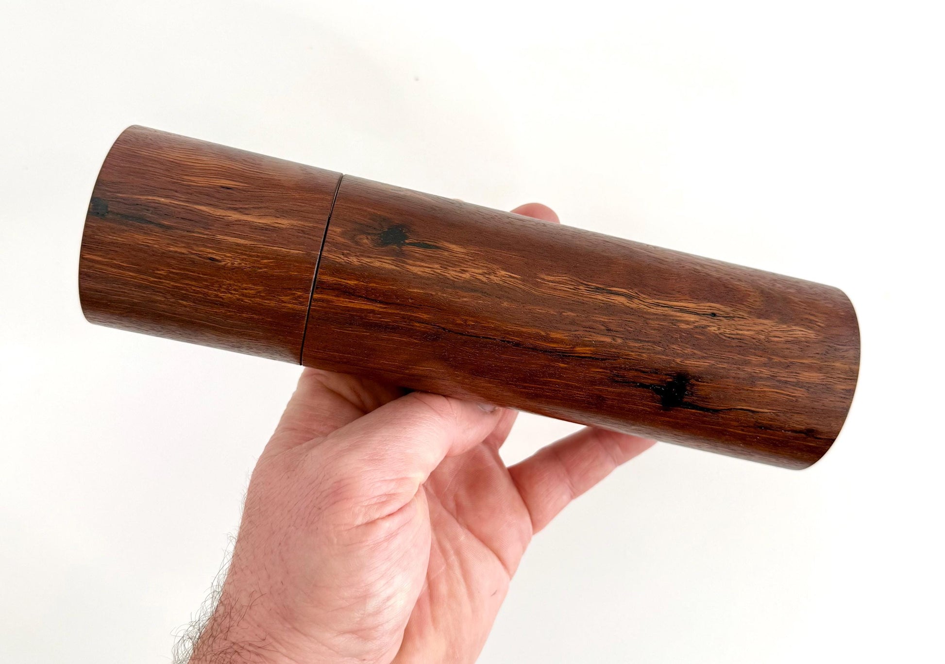 Mans hand holding single straight cylindrical Jarrah timber grinder