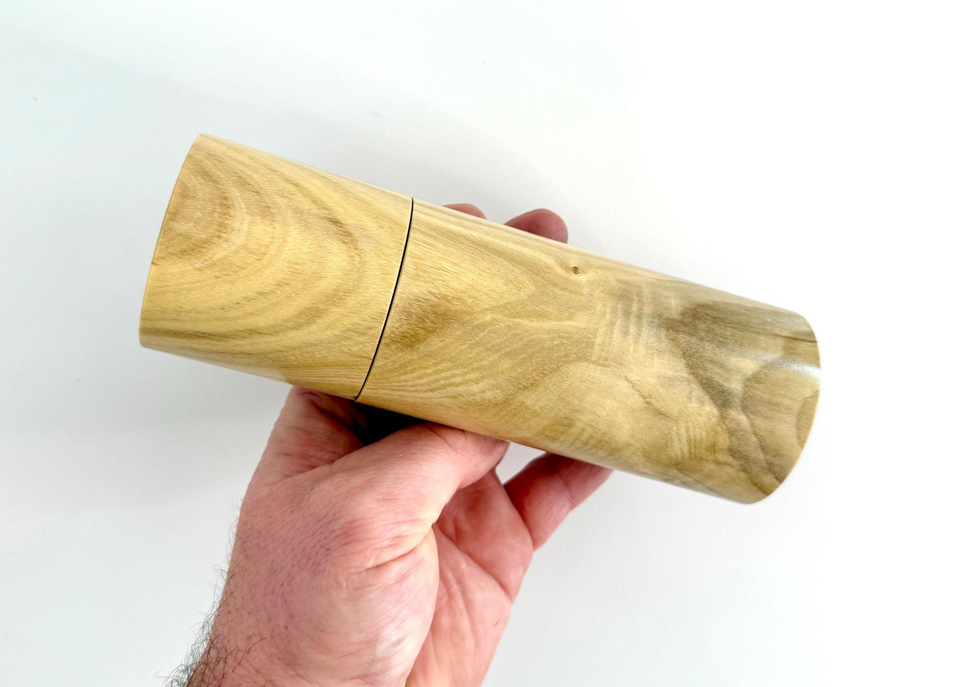 Mans hand holding single straight cylindrical Pistachio timber grinder