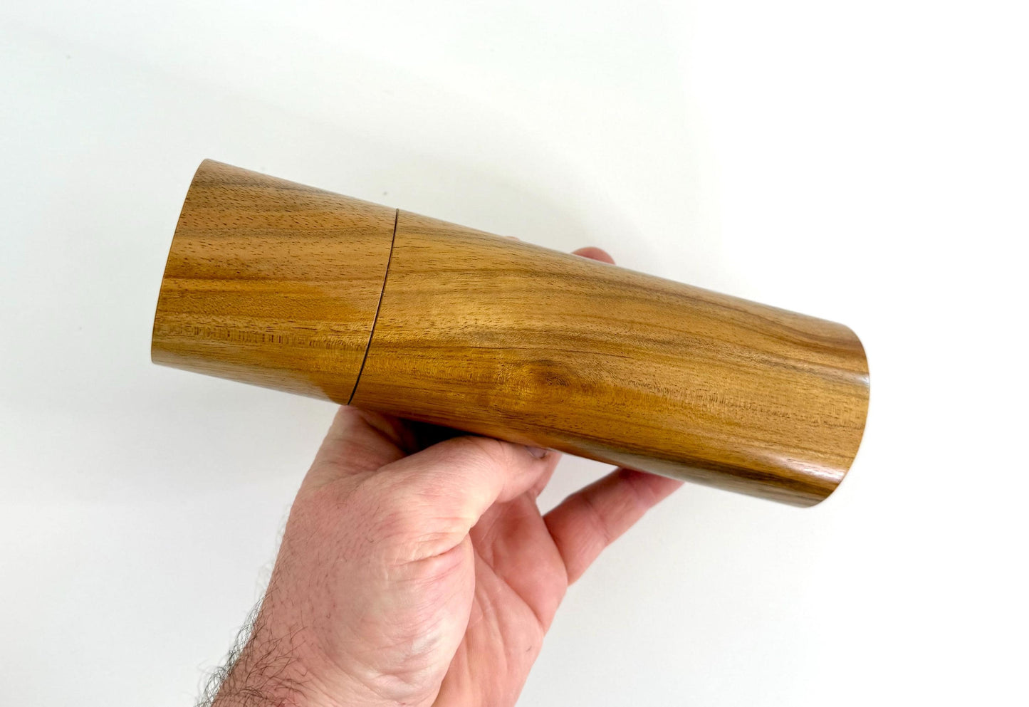 Mans hand holding single straight cylindrical Black Wattle timber grinder
