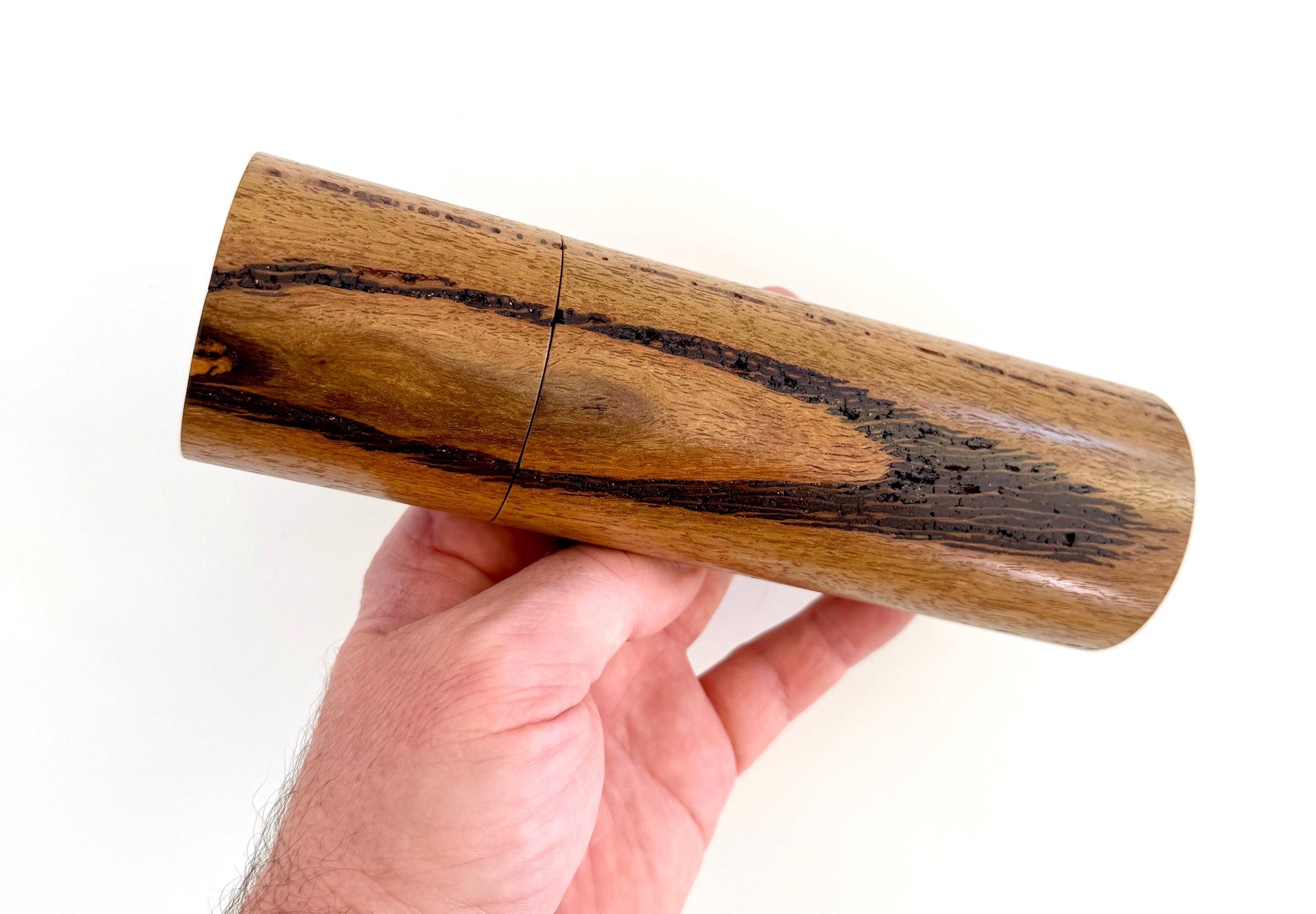 Mans hand holding single straight cylindrical Marri timber grinder